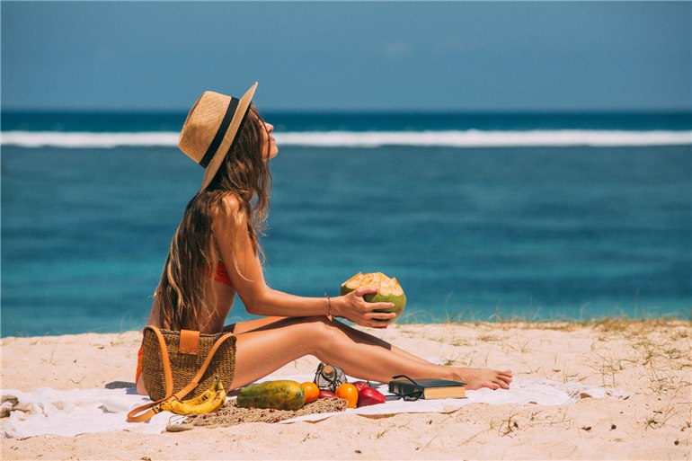 mulher sentada na areia segurando coco
